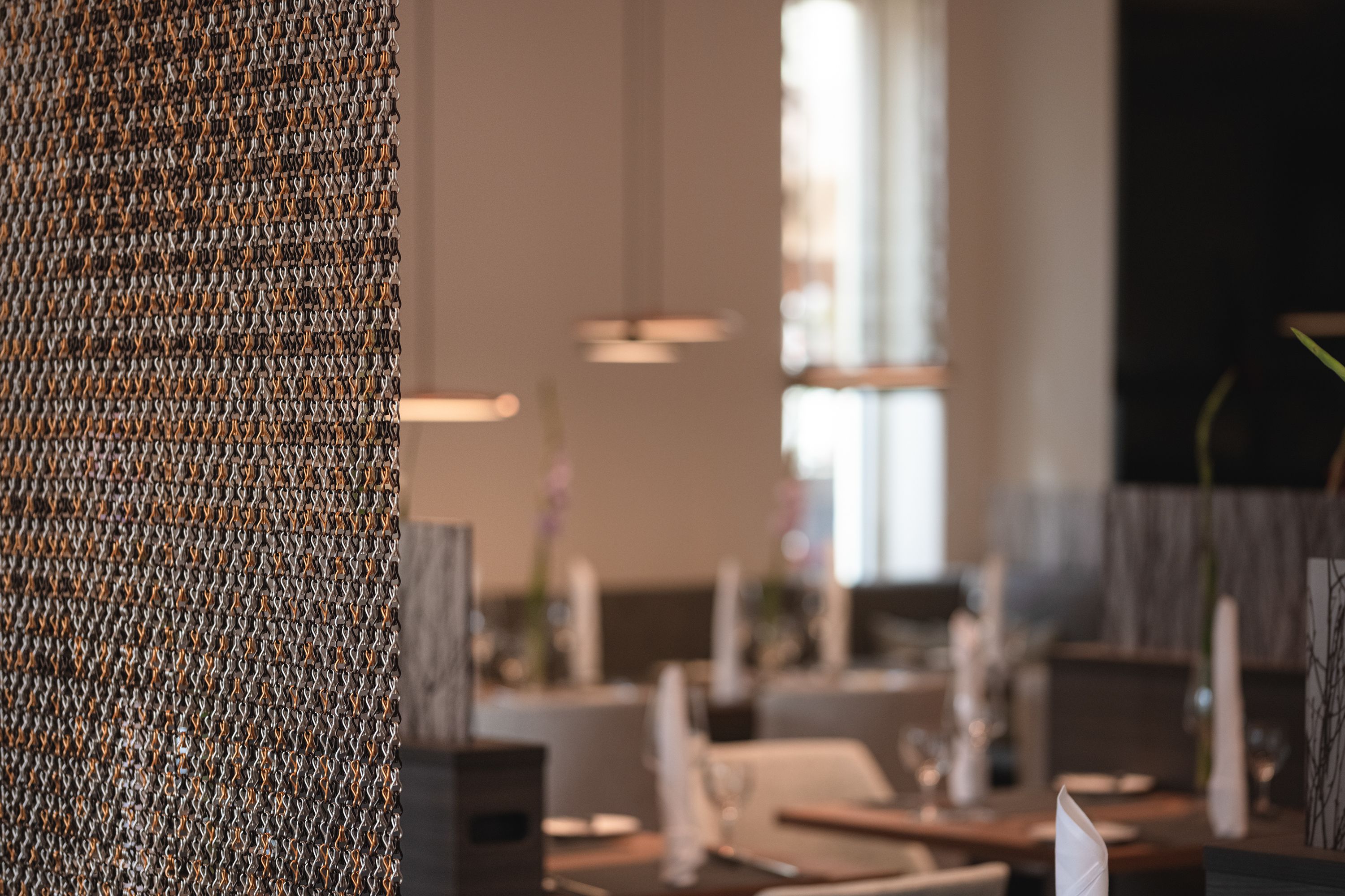 Interior de restaurante com destaque para uma parede texturizada e uma área de refeições desfocada.