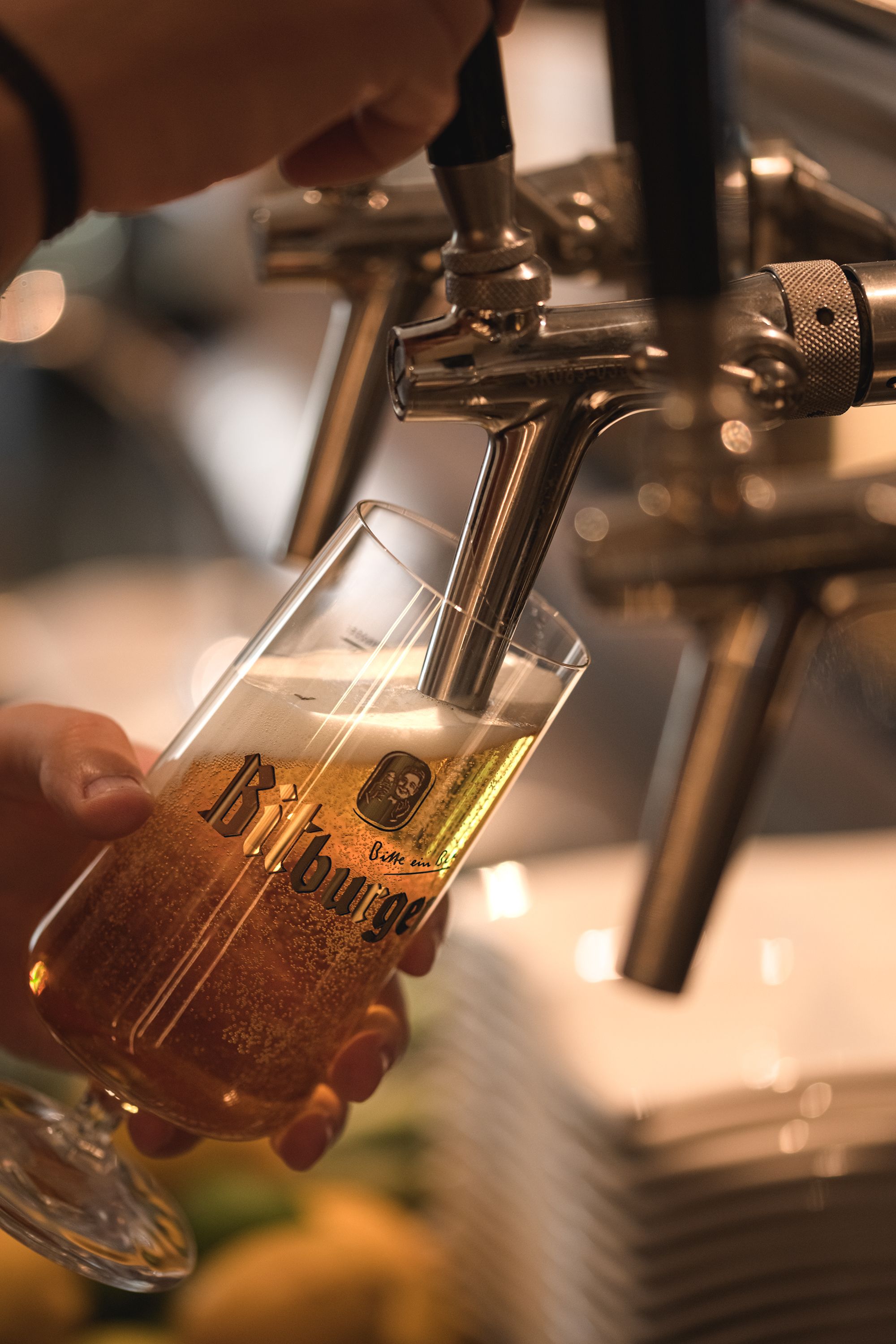 A hand holding a glass with a beer tap above it.
