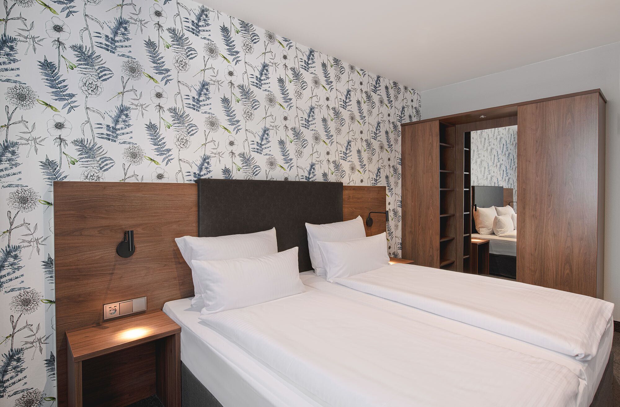 A neatly made bed with white linens, a wooden headboard, and a nightstand with a lamp.