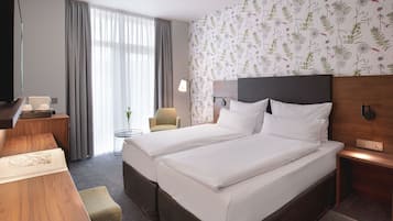 Habitación de hotel con cama doble, escritorio con lámpara, una silla y ventana con cortinas.