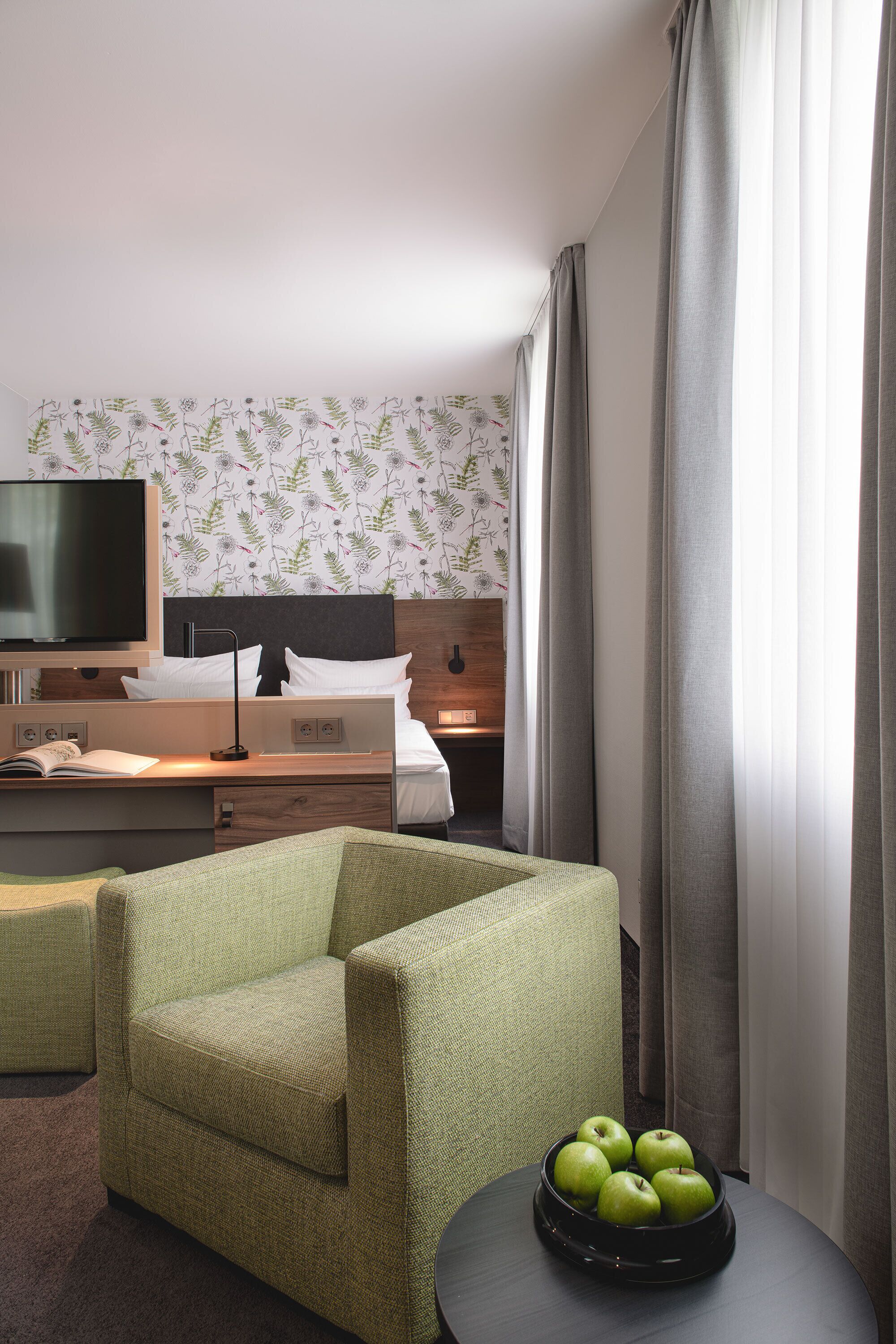 Una habitación de hotel con una cama, un escritorio, un televisor y un sillón verde.