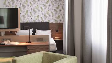 Una habitación de hotel con una cama, un escritorio, un televisor y un sillón verde.