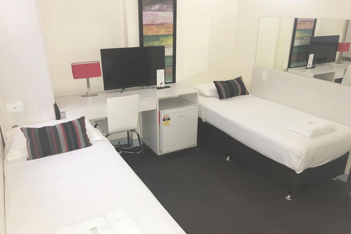 A hotel room with two single beds, a desk with a computer, a small fridge, a TV, and a mirror.