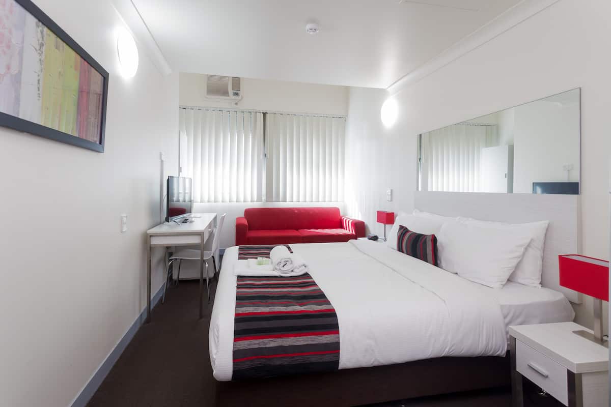 A hotel room with a bed, a desk, a red sofa, and a large mirror.