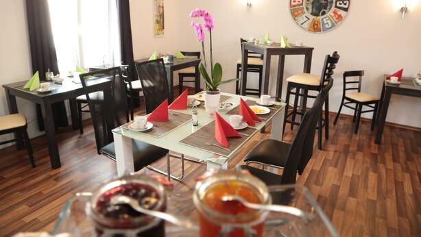 A dining area with tables set for meals, chairs, a decorative clock, and a potted plant. - Hotel am Marktplatz (Gangkofen)