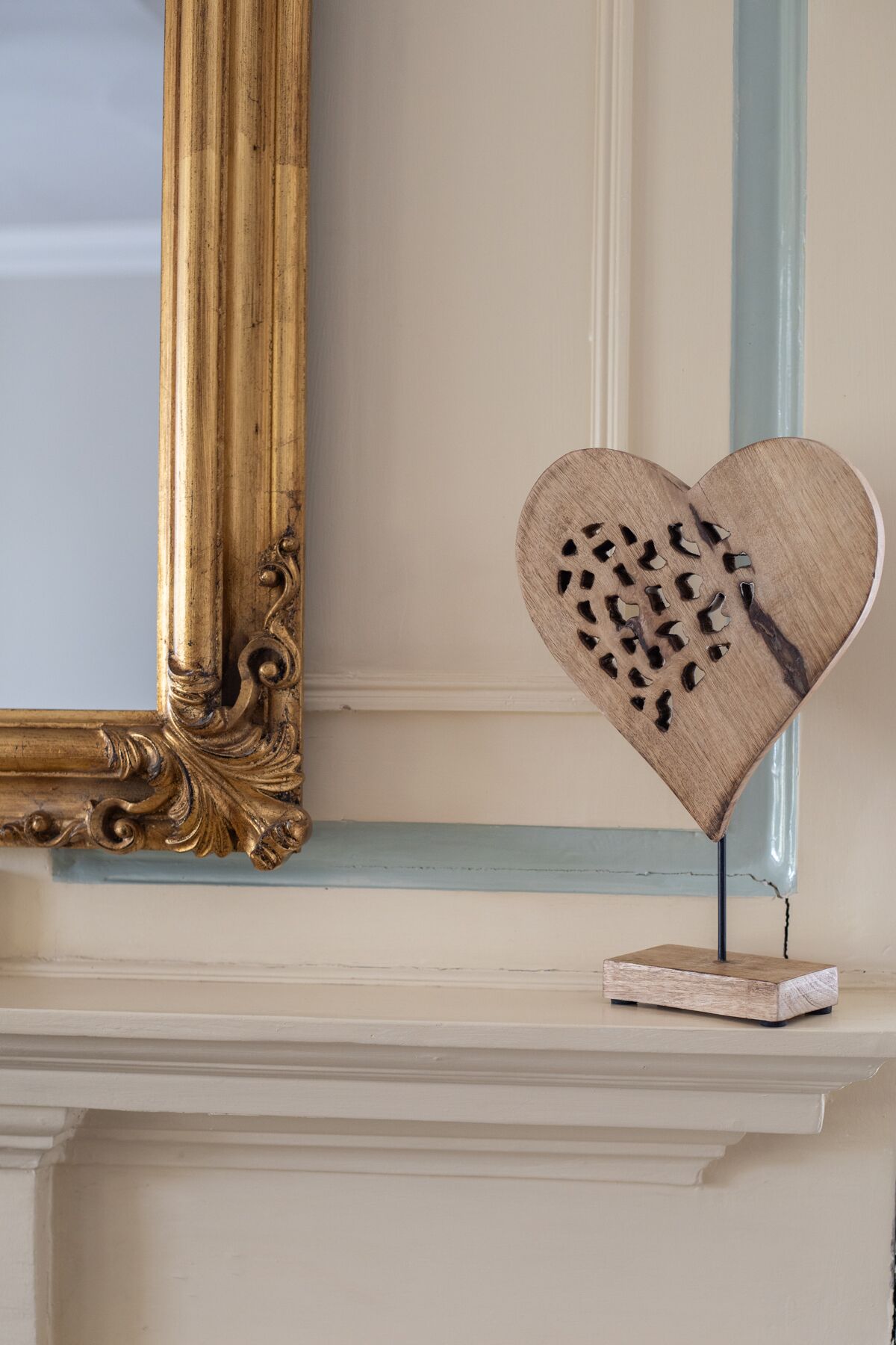 A decorative heart-shaped object with cut-out patterns on a mantelpiece.