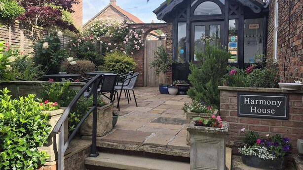 A brick house named 'Harmony House' with a stone staircase, outdoor seating, and a garden. - Harmony House (York)