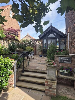 Une maison en briques appelée « Harmony House », dotée d’un escalier en pierre, d’un espace salon extérieur et d’un jardin.