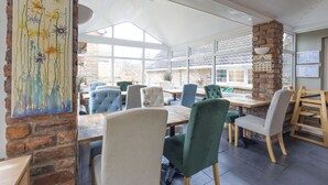 A spacious cafe with multiple seating areas, large windows, and a rustic brick wall. - Harmony House (York)