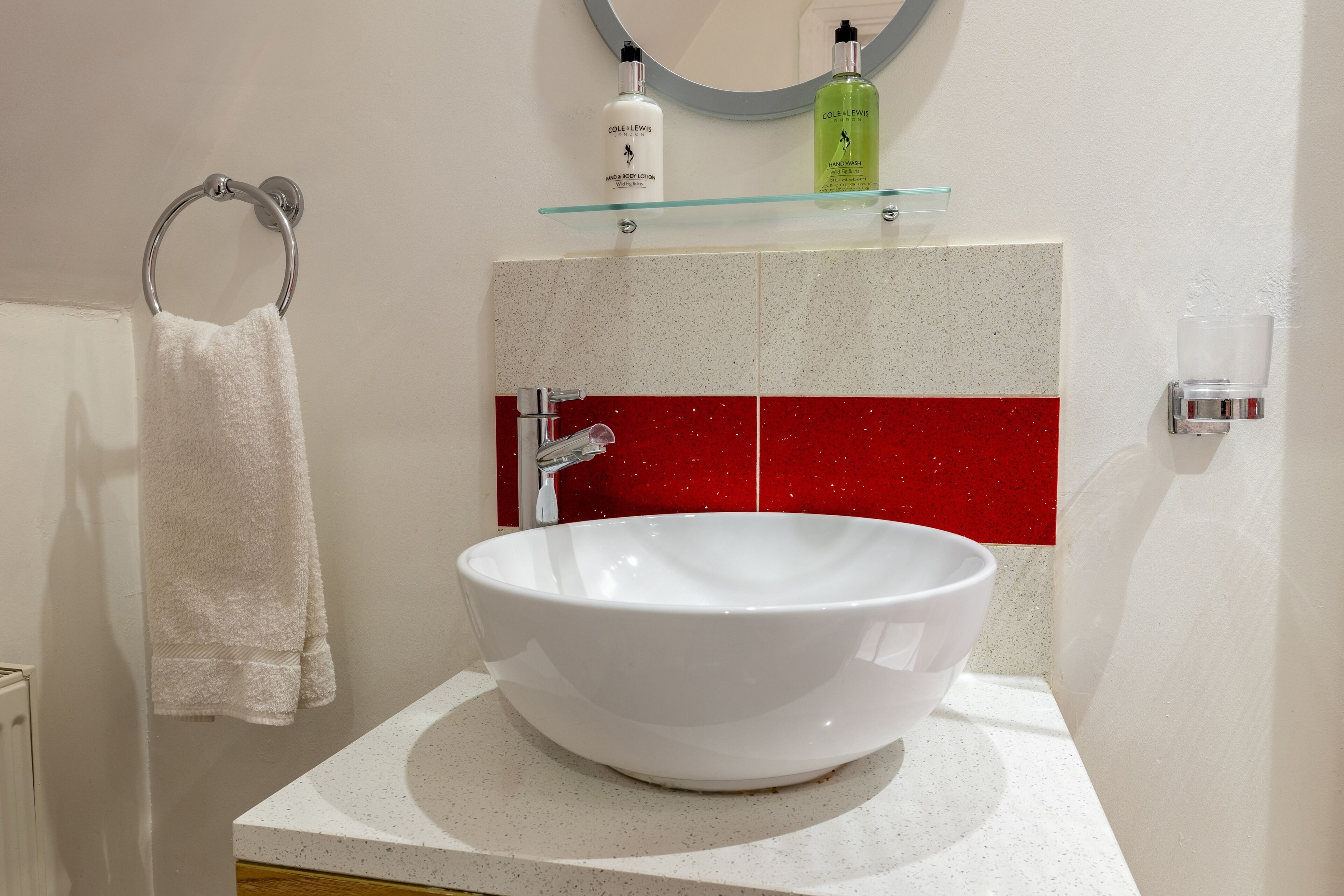 A bathroom with a white sink, a towel ring, and toiletries on a shelf.