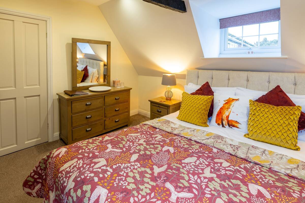 Quarto com cama grande, cômoda, mesa de cabeceira, abajur e janela com vista.
