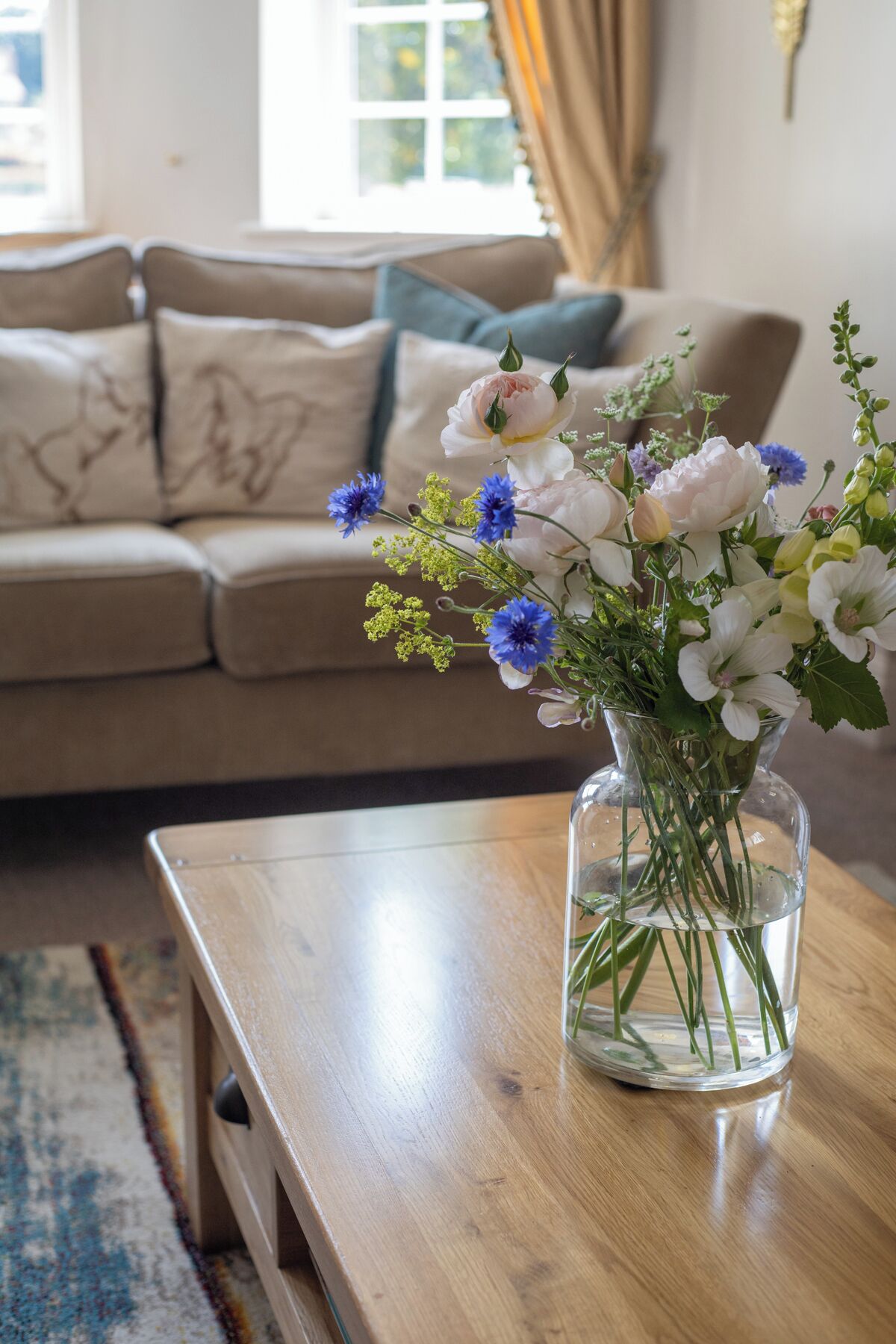 A living room with a sofa, a coffee table with a vase of flowers, and a window with curtains.