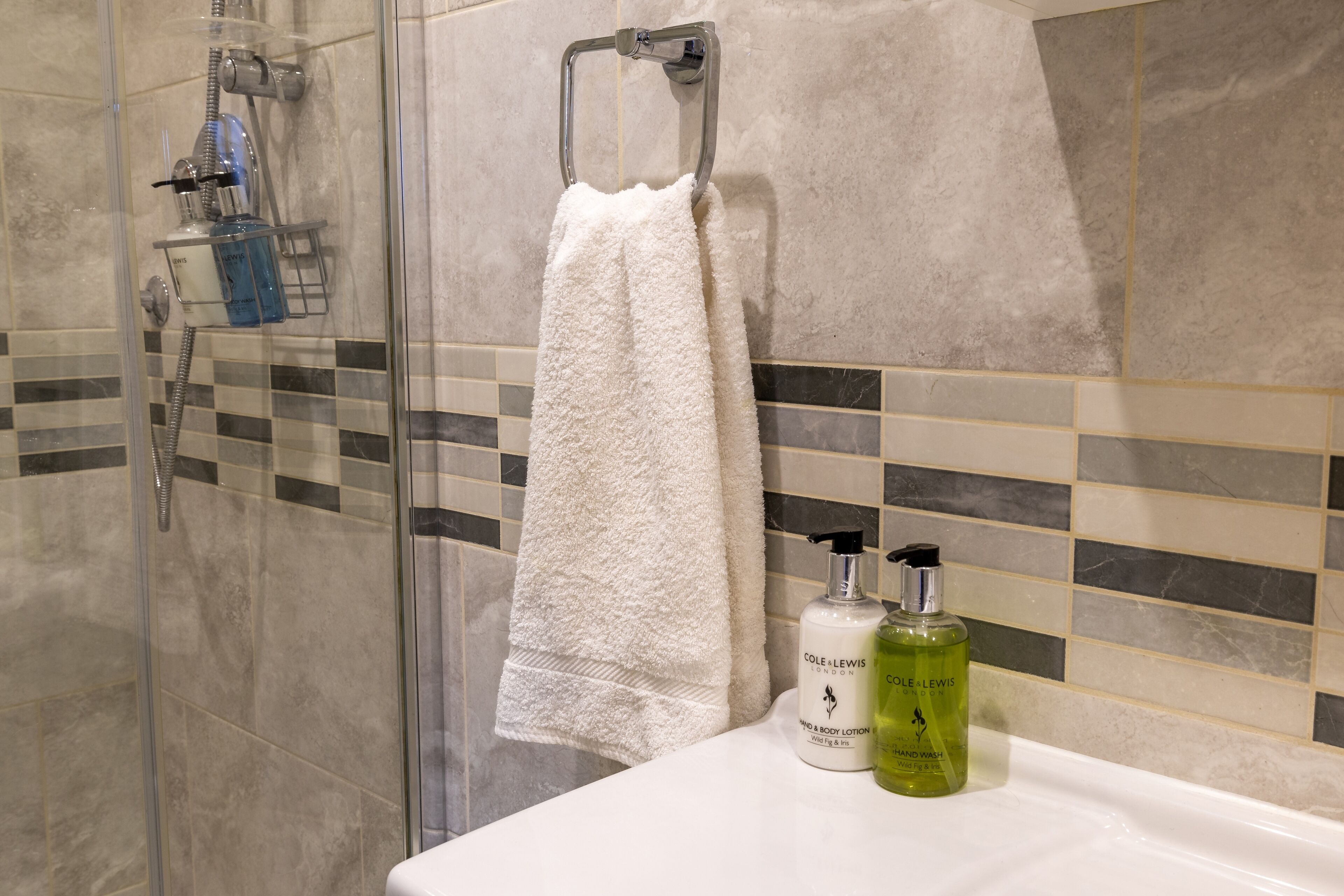 A bathroom with a glass shower enclosure, a white towel hanging on a metal rack, and two bottles of hand soap on the sink.