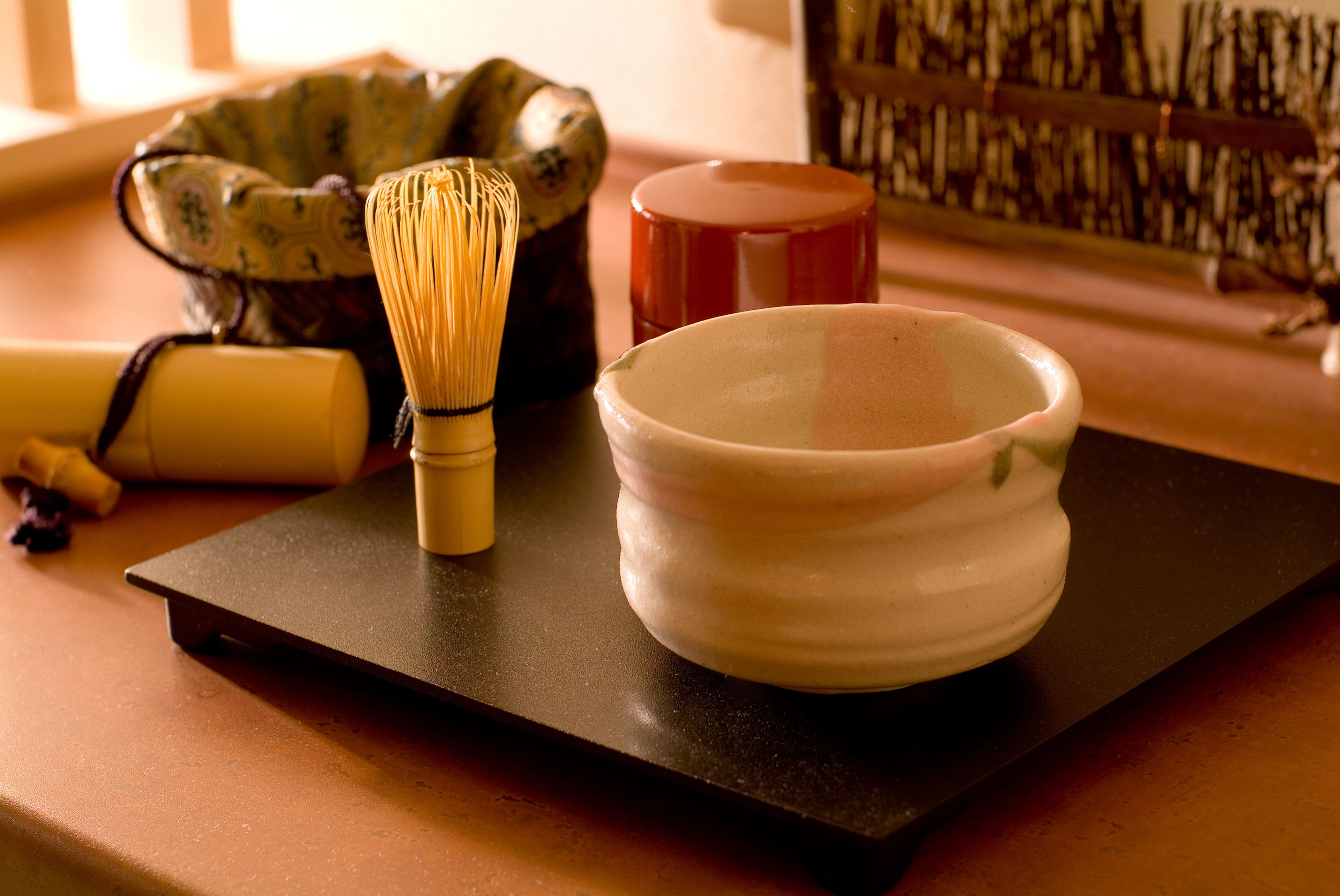 A traditional Japanese tea ceremony setup with a whisk, bowl, and a decorative container on a black tray.