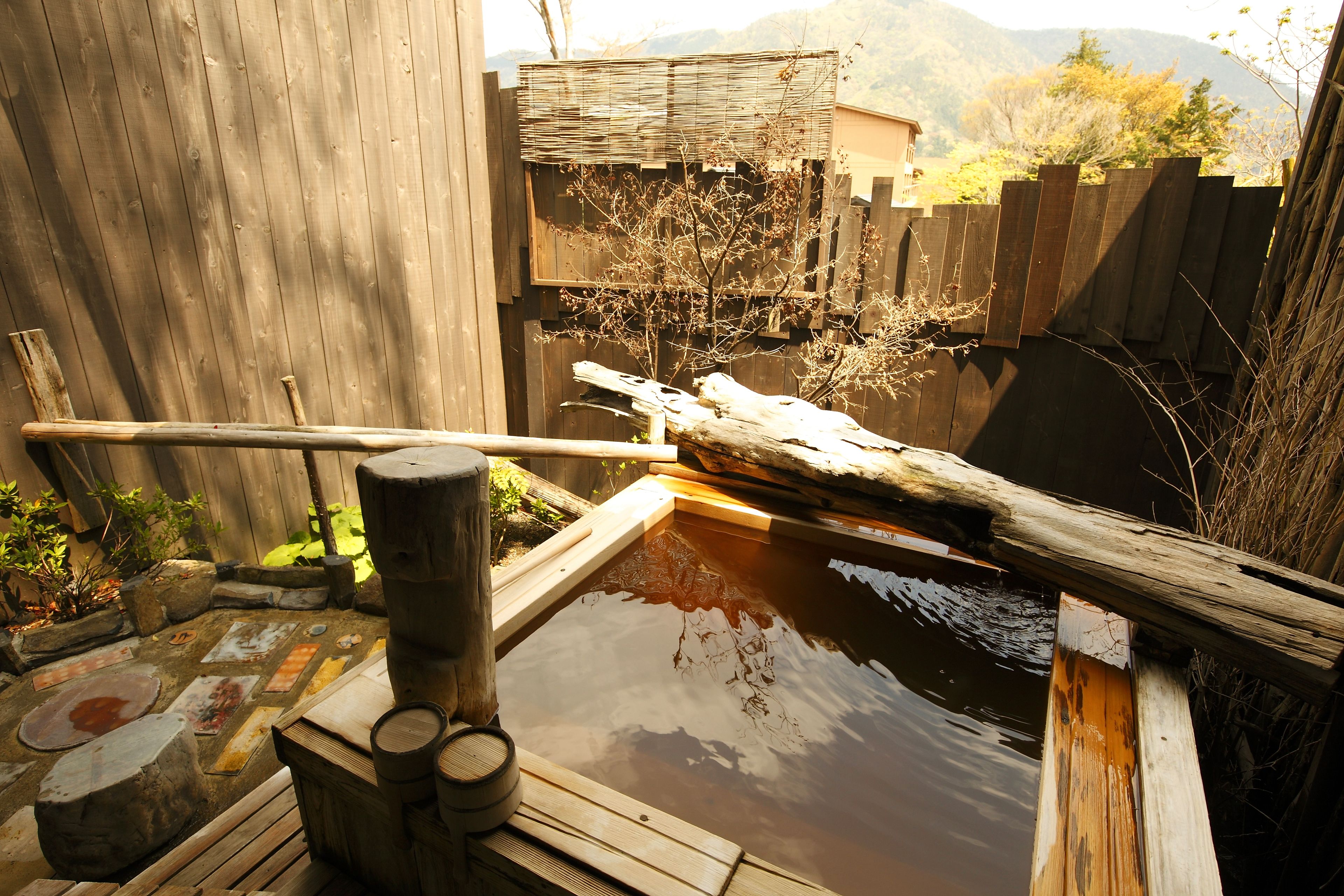 A wooden outdoor hot spring area with a wooden deck, a wooden fence, and a wooden structure over the water.
