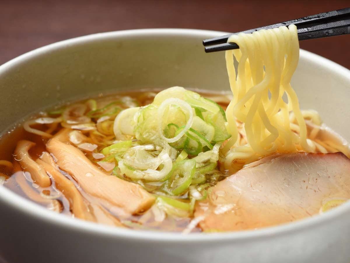 Een kom ramen met noedels, plakjes vlees en groene uien.