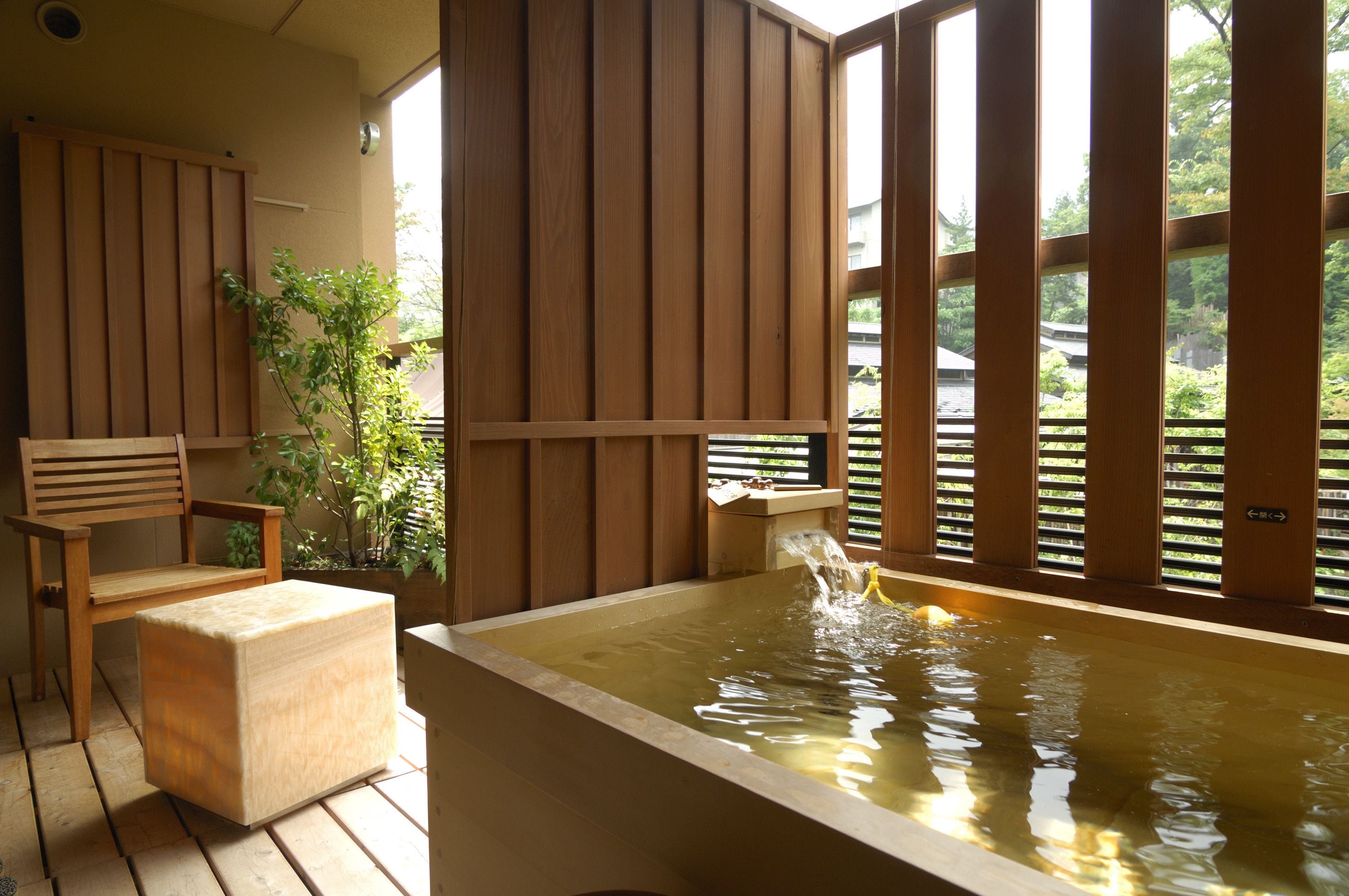 Una bañera de madera con un elemento acuático, una silla de madera y una pequeña mesa con un lavabo.