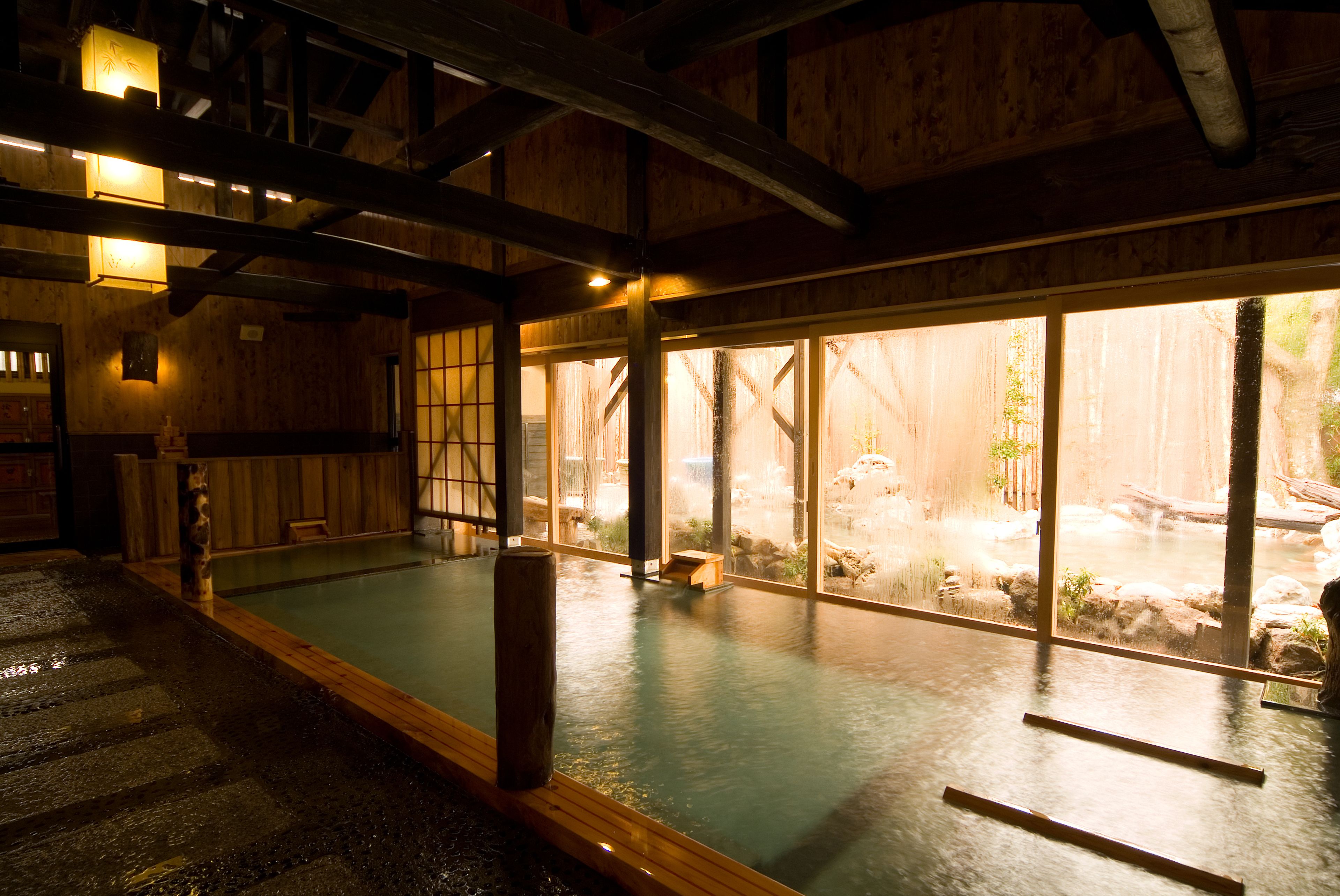 A traditional Japanese onsen with wooden interiors and a view of an outdoor hot spring area.