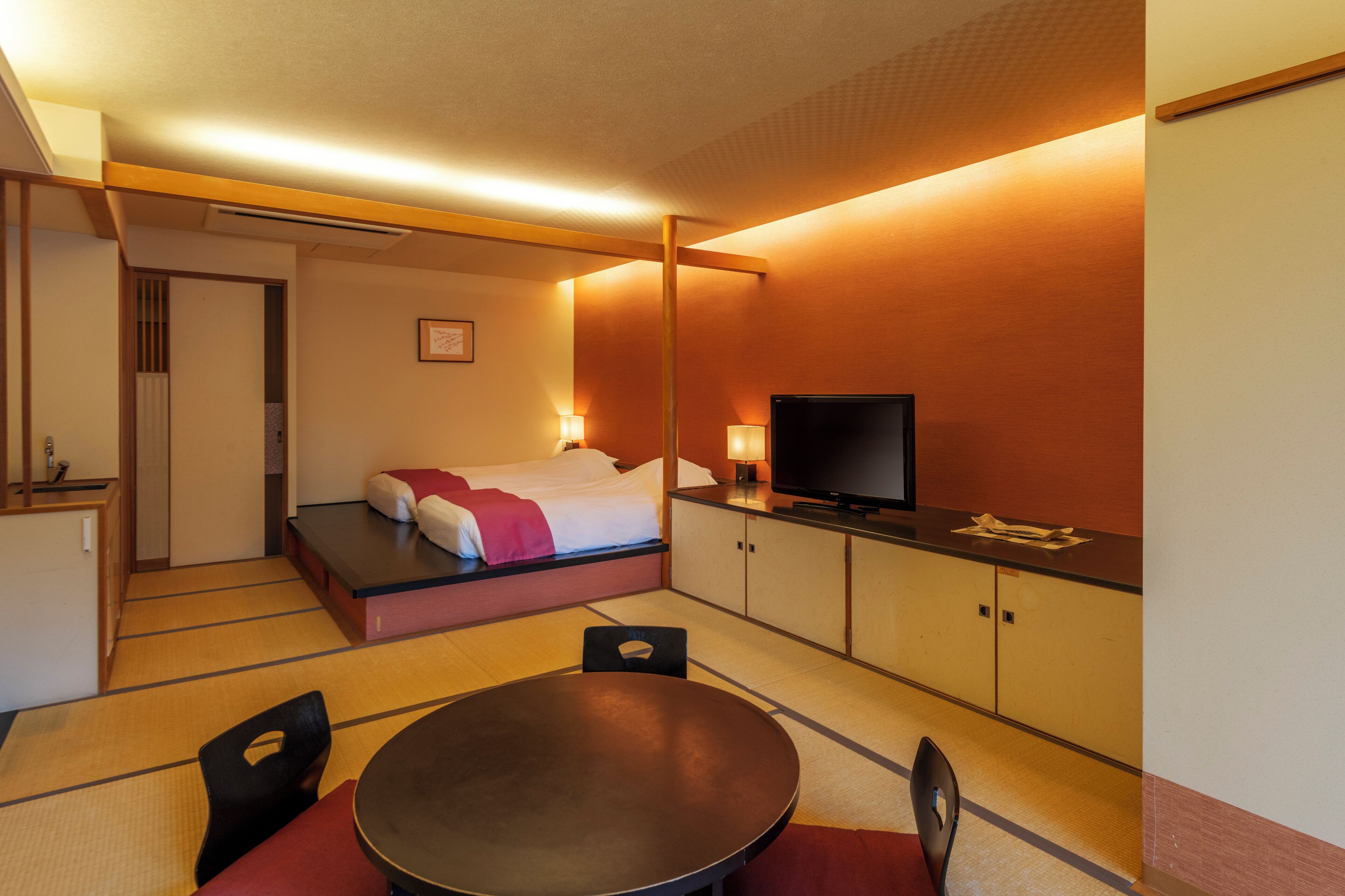 A hotel room with a bed, a television, a dining table, and a small kitchen area.