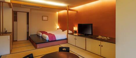 Habitación de hotel con cama, televisión, mesa de comedor y pequeña cocina.
