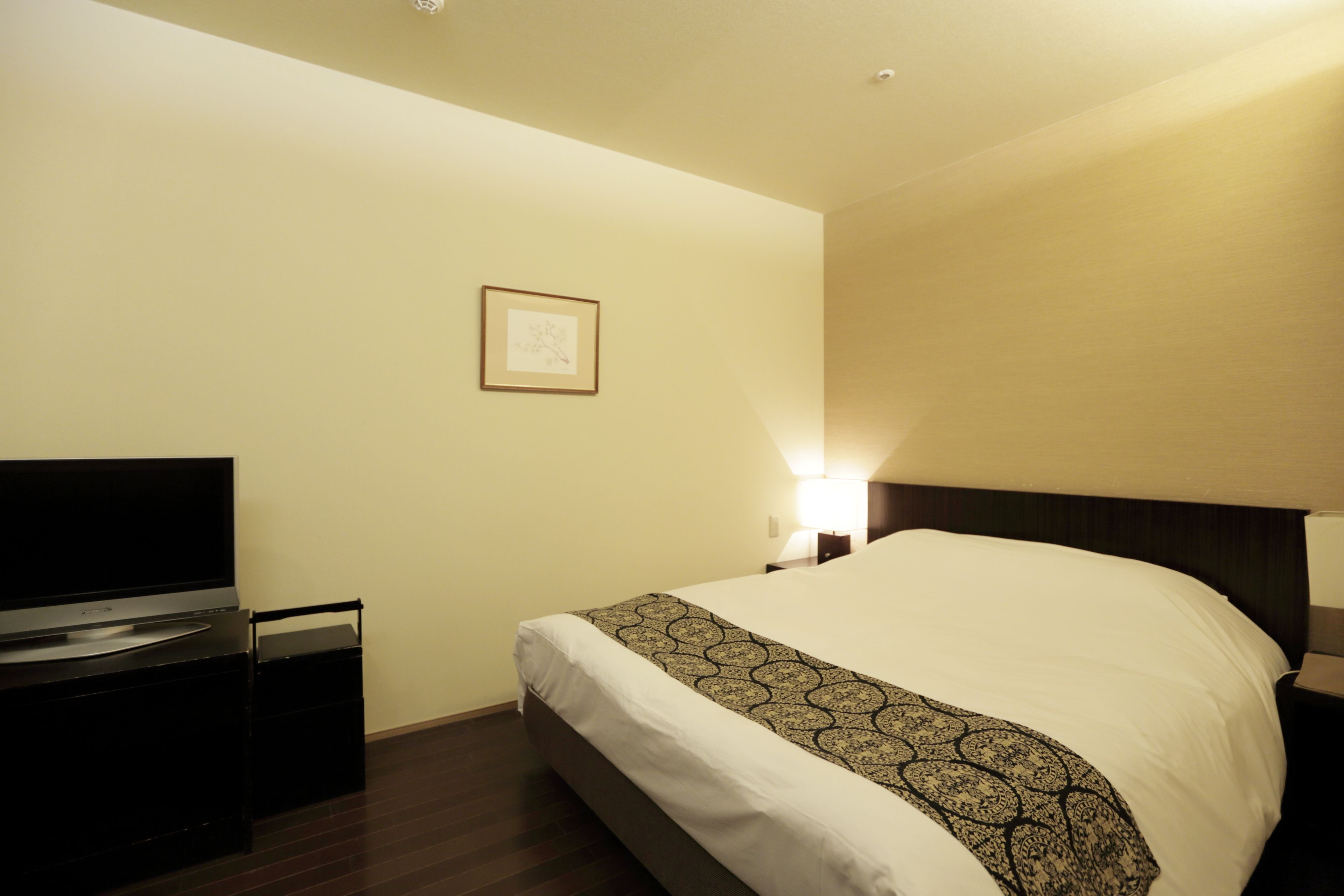 A hotel room with a bed, a TV, and a nightstand with a lamp.