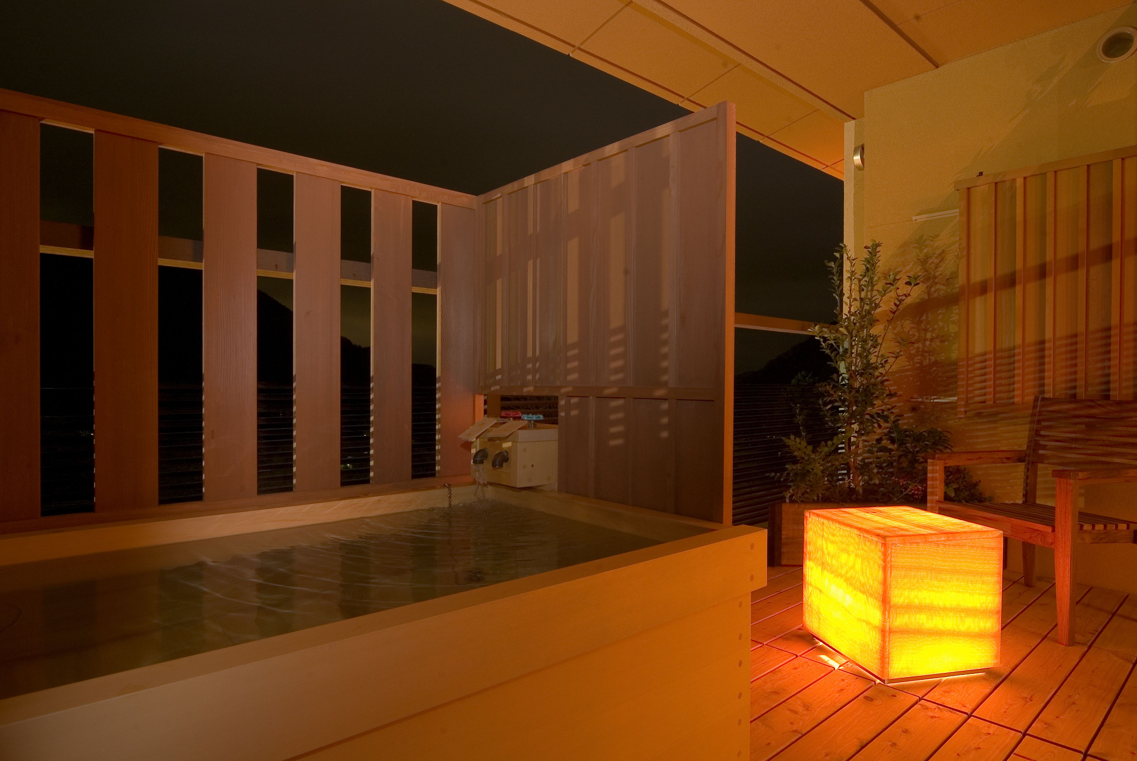 Un espace moderne pour jacuzzi extérieur, doté d’une terrasse en bois, d’un jacuzzi protégé par des parois de verre et d’un luminaire en bois.