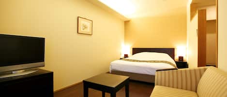 A hotel room with a bed, a TV on a stand, a small table, and a sofa.