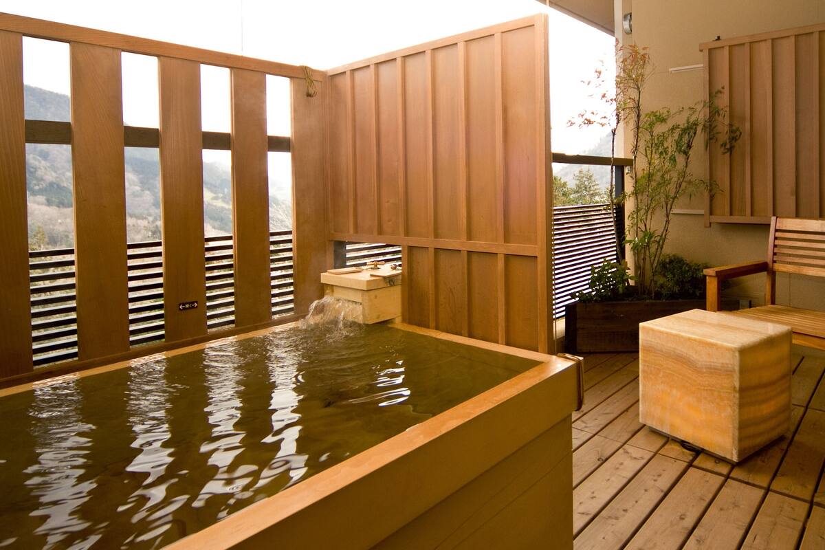 A wooden deck with a hot tub, wooden benches, and a view of a mountainous landscape.