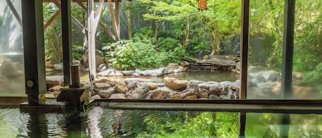 Un jardín interior tranquilo con un estanque, estructuras de madera y abundante vegetación.