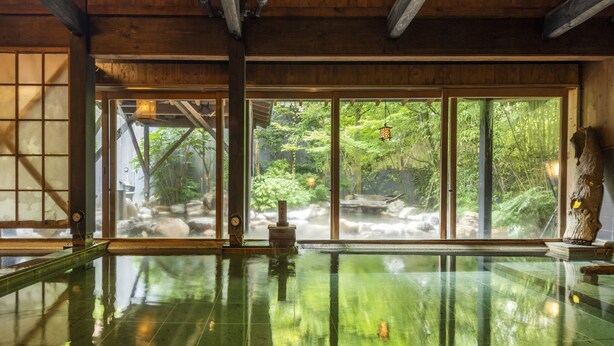 Un onsen japonés tradicional con interiores de madera, un amplio ventanal con vistas a un paisaje natural y una cuenca de piedra en el centro.