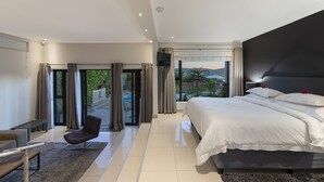 A modern bedroom with a large bed, a chair, and a view of a swimming pool. - THEBLOEM Guest Suites by Knysna Paradise Collection (Knysna)