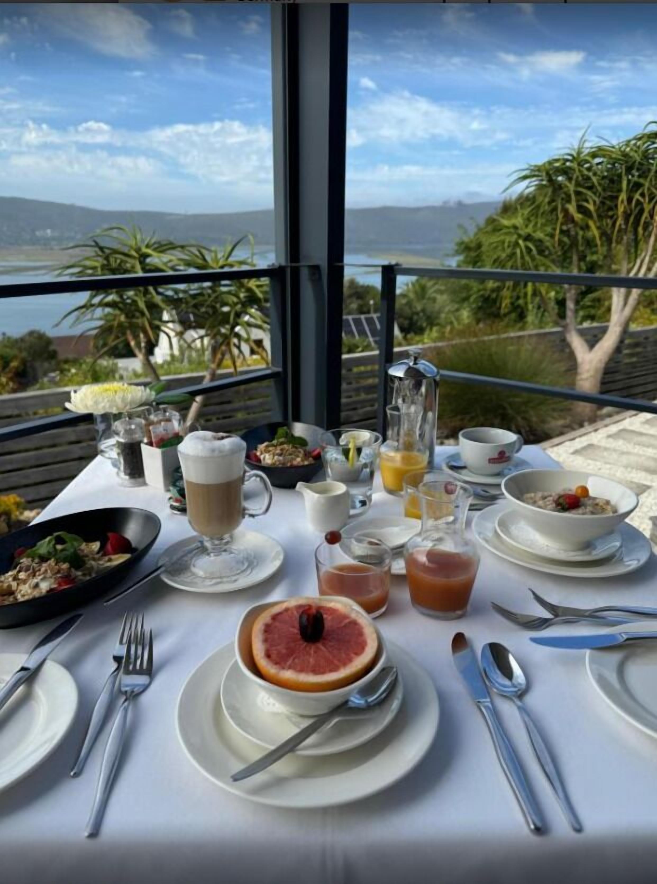 A table set for breakfast with various dishes, drinks, and a view of the ocean.