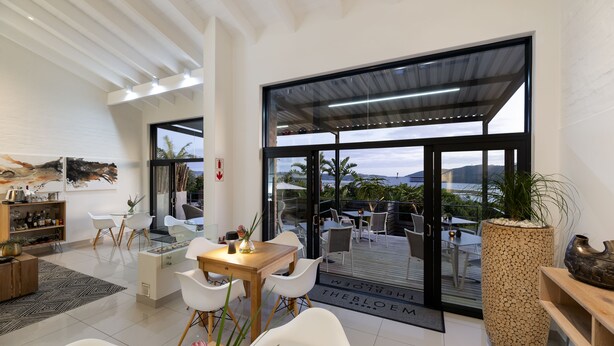 A modern living room with a wooden dining table, white chairs, and a large potted plant. - THEBLOEM Guest Suites by Knysna Paradise Collection (Knysna)
