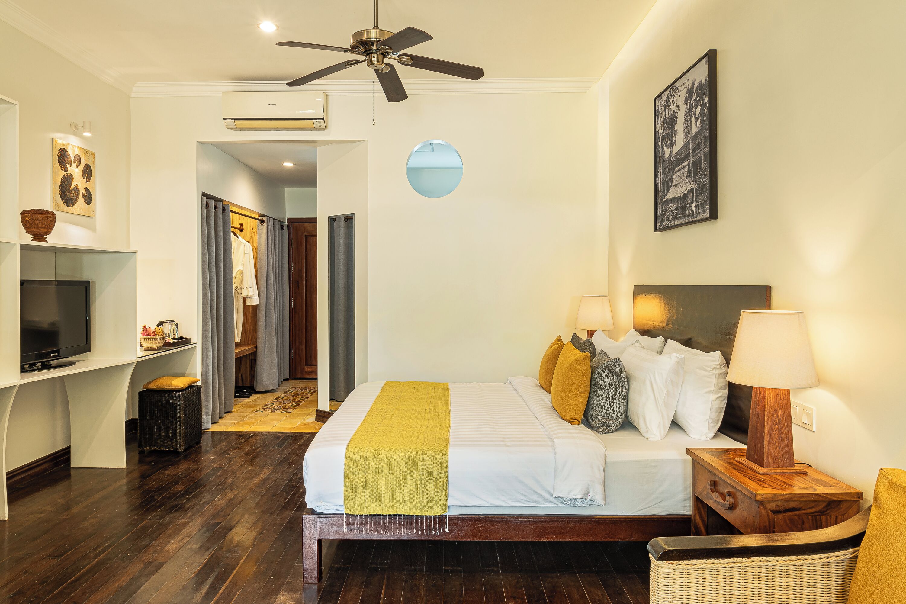 A hotel room with a bed, a TV, a ceiling fan, a wall-mounted air conditioner, and a framed picture.