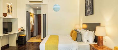 A hotel room with a bed, a TV, a ceiling fan, a wall-mounted air conditioner, and a framed picture.