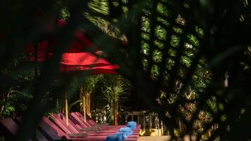 A row of sun loungers with towels, surrounded by lush greenery and a red umbrella.