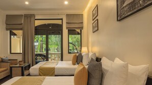 A hotel room with two beds, a sofa, a small table, and a view of greenery outside. - Pavillon d'Orient Boutique (Siem Reap)