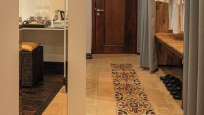 A hotel hallway with a wooden door, a mirror, a tray with toiletries, a patterned rug, and a wooden bench with slippers. - Pavillon d'Orient Boutique (Siem Reap)