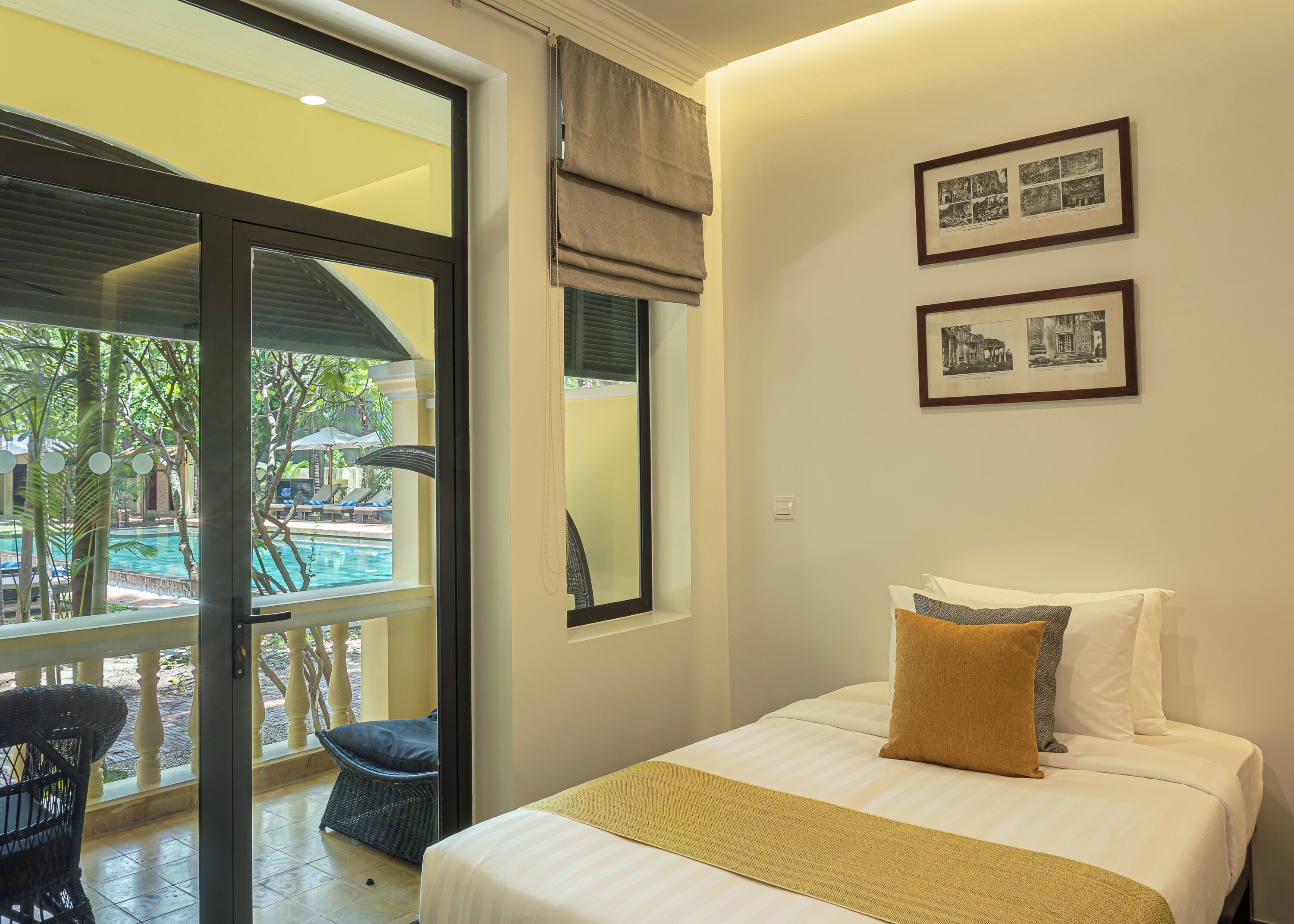 Une chambre d’hôtel avec un lit, une vue sur la piscine et deux tableaux encadrés au mur.