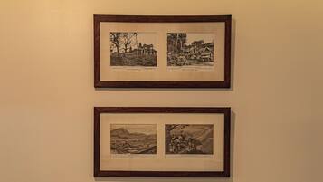 A neatly made bed with white and brown pillows, a framed picture above it, and a plain wall.