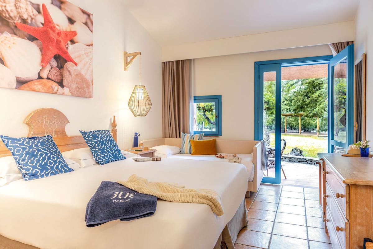 A hotel room with a large bed, a desk, a chair, and a view of the garden.