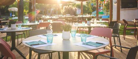 An outdoor dining area with round tables and chairs, some with potted plants.