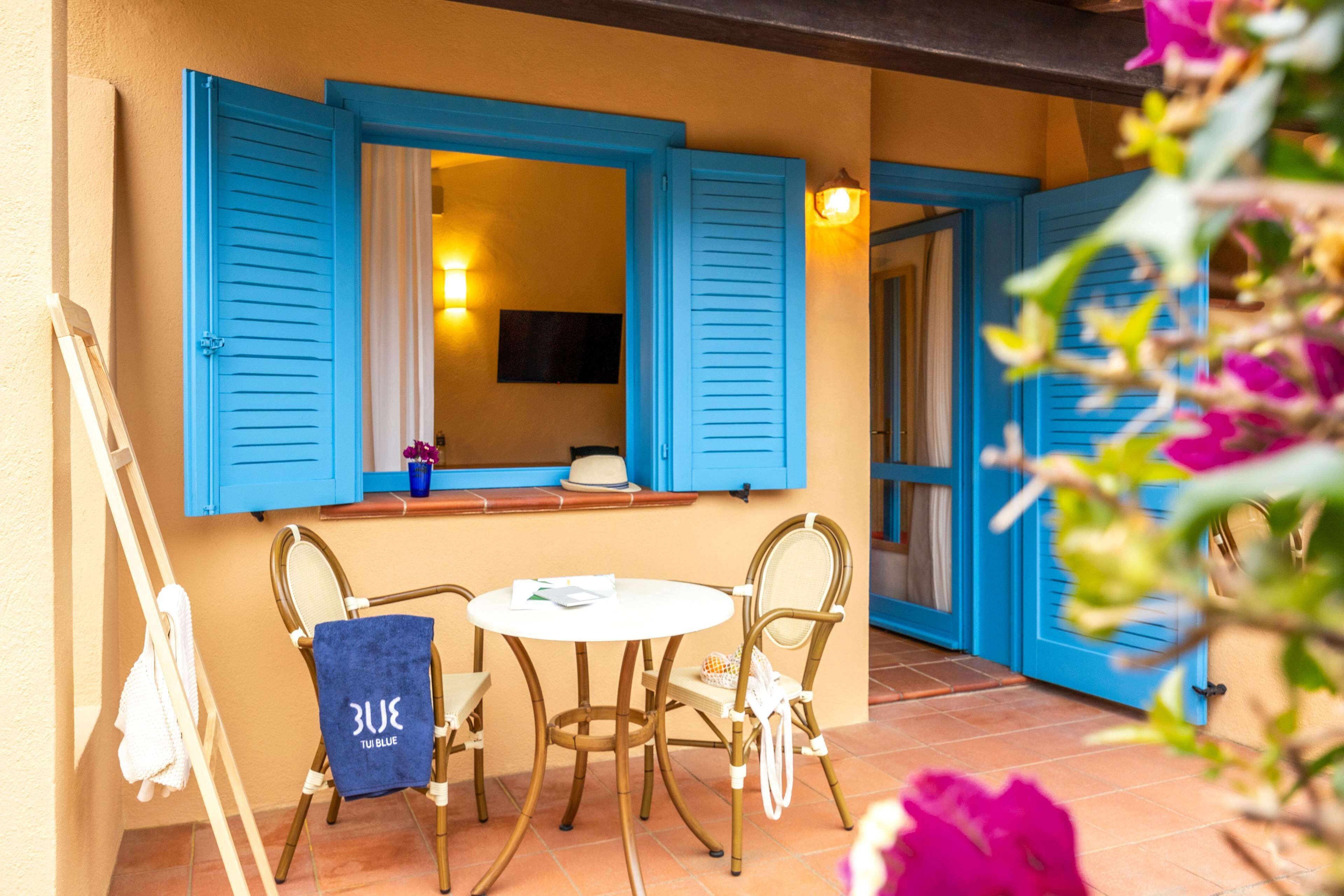 Une terrasse avec une table et des chaises, un porte-serviettes et une fenêtre avec des volets bleus.