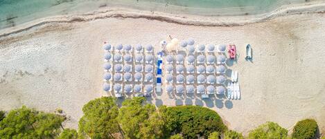 An aerial view of a beach with rows of umbrellas and beach chairs, a lifeguard tower, and a rocky shoreline.