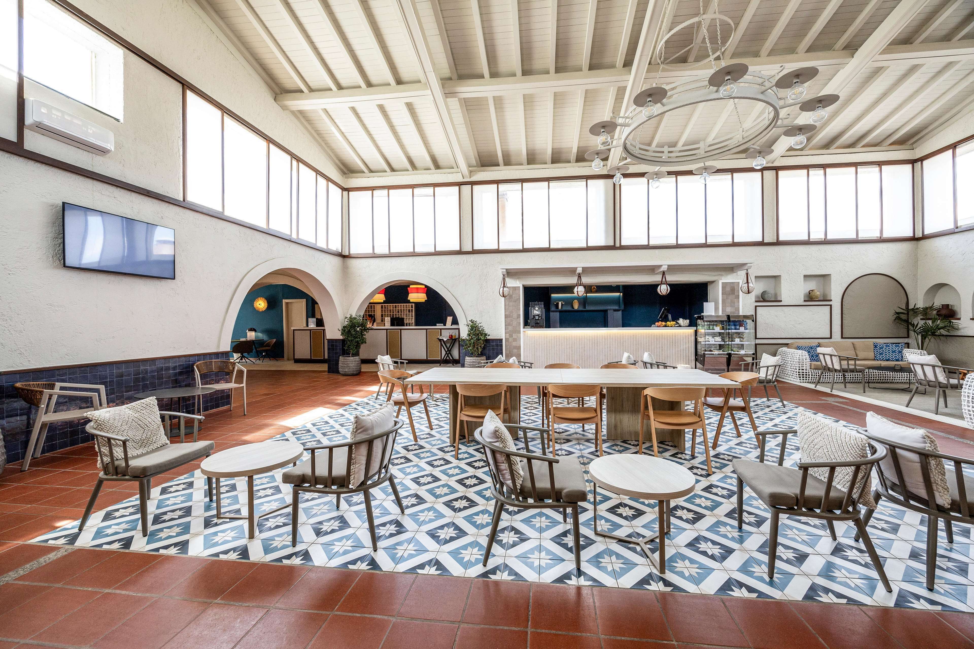 Un amplio espacio interior con techo alto, ventanas grandes y una mesa de comedor central rodeada de sillas.
