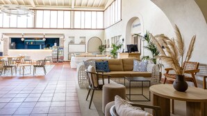 A spacious lobby with a high ceiling, a reception desk, seating areas, and a view through an arched doorway. - TUI BLUE Budoni (Budoni)