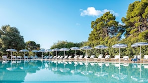 A pool with lounge chairs and umbrellas, surrounded by trees. - TUI BLUE Budoni (Budoni)