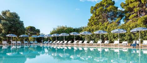 Una piscina con sillas de descanso y sombrillas, rodeada de árboles.