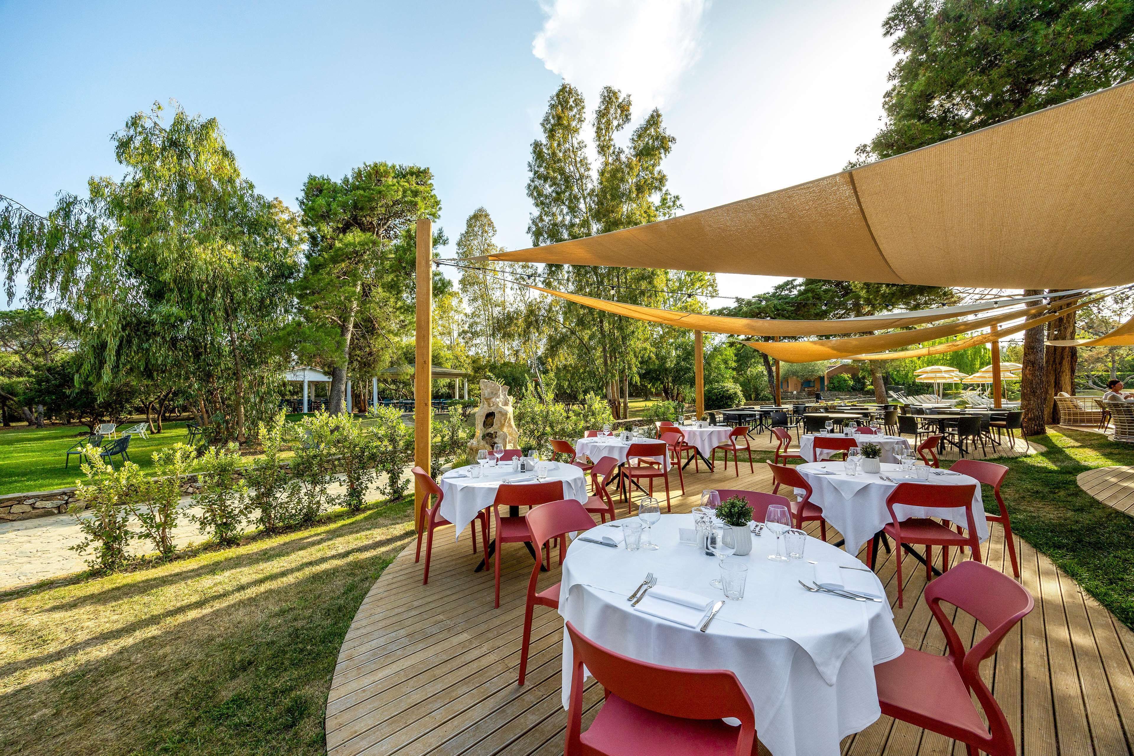 Un espace de restauration en plein air avec des tables rondes et des chaises rouges, entouré d’arbres et d’une terrasse en bois.