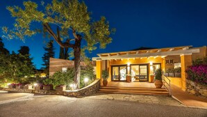 A modern hotel entrance with a stone staircase leading up to the door, surrounded by potted plants and a large tree. - TUI BLUE Budoni (Budoni)